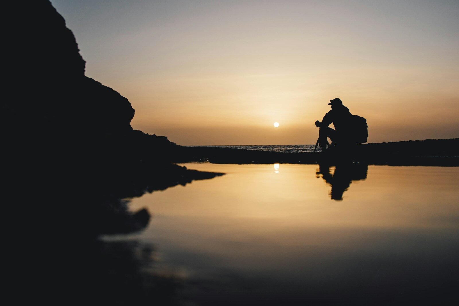 a man sitting on a rock next to a body of water