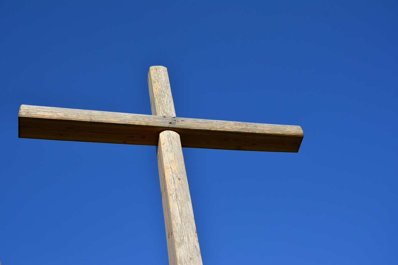 Cruz simples de madeira destacada sob céu dourado no nascer do sol