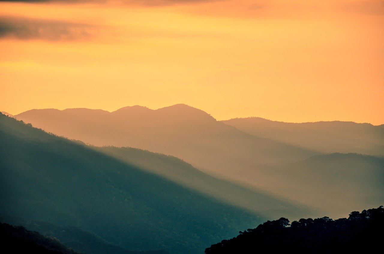 Pôr do sol suave com tons alaranjados e silhueta de colinas serenas