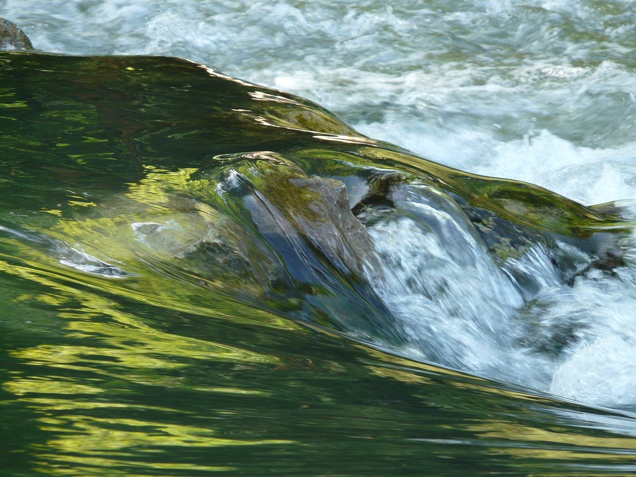 Rio límpido com águas correndo harmoniosamente entre pedras arredondadas e floresta verde