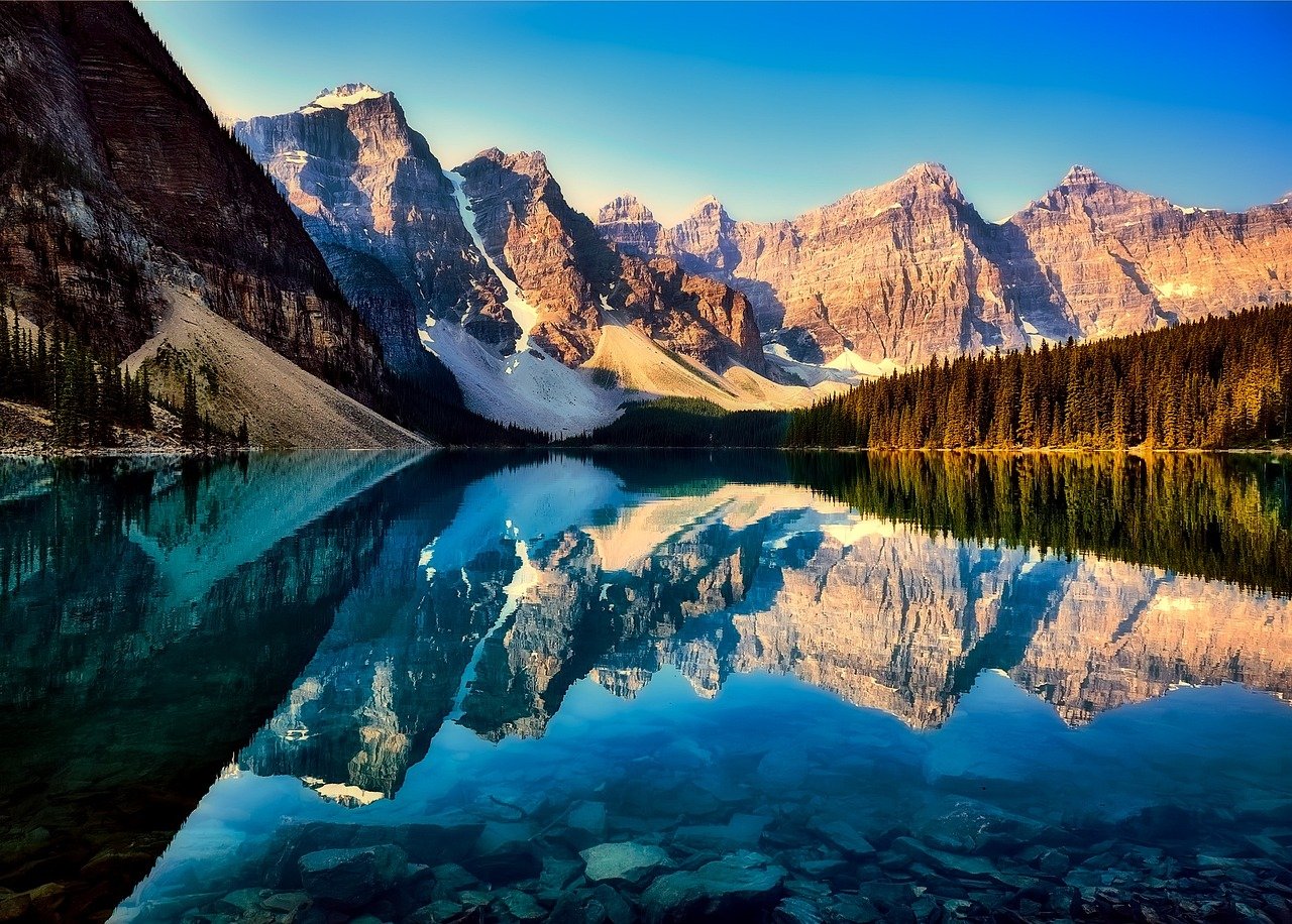 Lago sereno cercado por montanhas verdejantes refletindo o céu límpido e o sol dourado